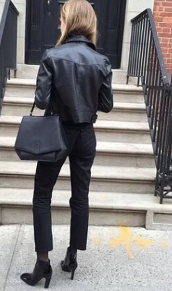 Mujer vestida con un pantalón mom fit negro, una bolsa de mano negra de cuero y una chamarra de piel con botines frente a una escalera 
