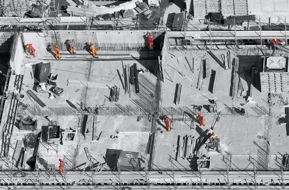 Imagen aérea de la construcción del techo de un edificio, en blanco y negro, con doce trabajadores resaltados en color naranja